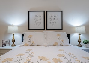 A neatly made bed with floral bedding, two framed inspirational quotes on the wall, and two bedside lamps.