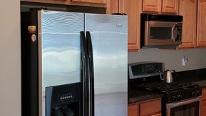Une cuisine équipée d’un réfrigérateur en acier inoxydable, d’un four à micro-ondes, d’une cuisinière et de meubles de rangement en bois.