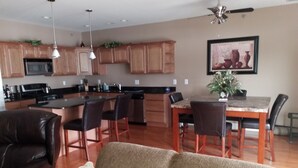 Une cuisine moderne avec des meubles en bois, un coin repas comprenant une table et des chaises, et un salon avec un canapé et des coussins décoratifs.