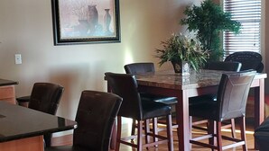 Un coin repas avec une table en bois, quatre chaises, un ventilateur de plafond et un tableau encadré au mur.