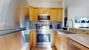A modern kitchen with stainless steel appliances, wooden cabinets, a stone backsplash, and a large window.