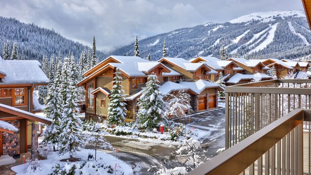 Ein mit Schnee bedecktes Chalet mit Holzhütten, eine Skipiste im Hintergrund und freie Sicht auf die Berge.
