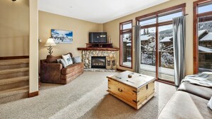 Ein gemütliches Wohnzimmer mit Kamin, Fernseher und einem großen Fenster mit Blick auf Schnee.