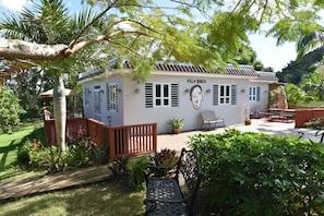 Villa Bonita, un edifici blanc amb teulada d'àmples rajoles, envoltat de vegetació exuberant i una terrassa de fusta.