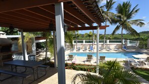 A covered outdoor area with a pool, lounge chairs, and a barbecue setup.