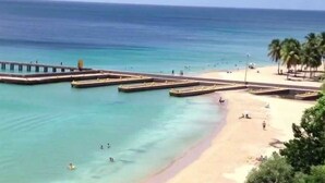 A beach with a pier extending into the water, a sandy shore, and palm trees. - Sleeps 12 apartment #7, pool, jacuzzi, beautiful property (AGUADILLA)
