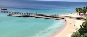 Una platja amb un moll que s'endinsa a l'aigua, una riba sorrenca i palmeres.