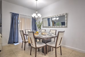 A dining room with a rectangular table, six chairs, a chandelier, and a large mirror on the wall.