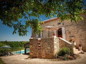 A stone building with a pool, outdoor seating, and a staircase leading to a wooden door. - Holiday home with private pool and views (Montcabrier)