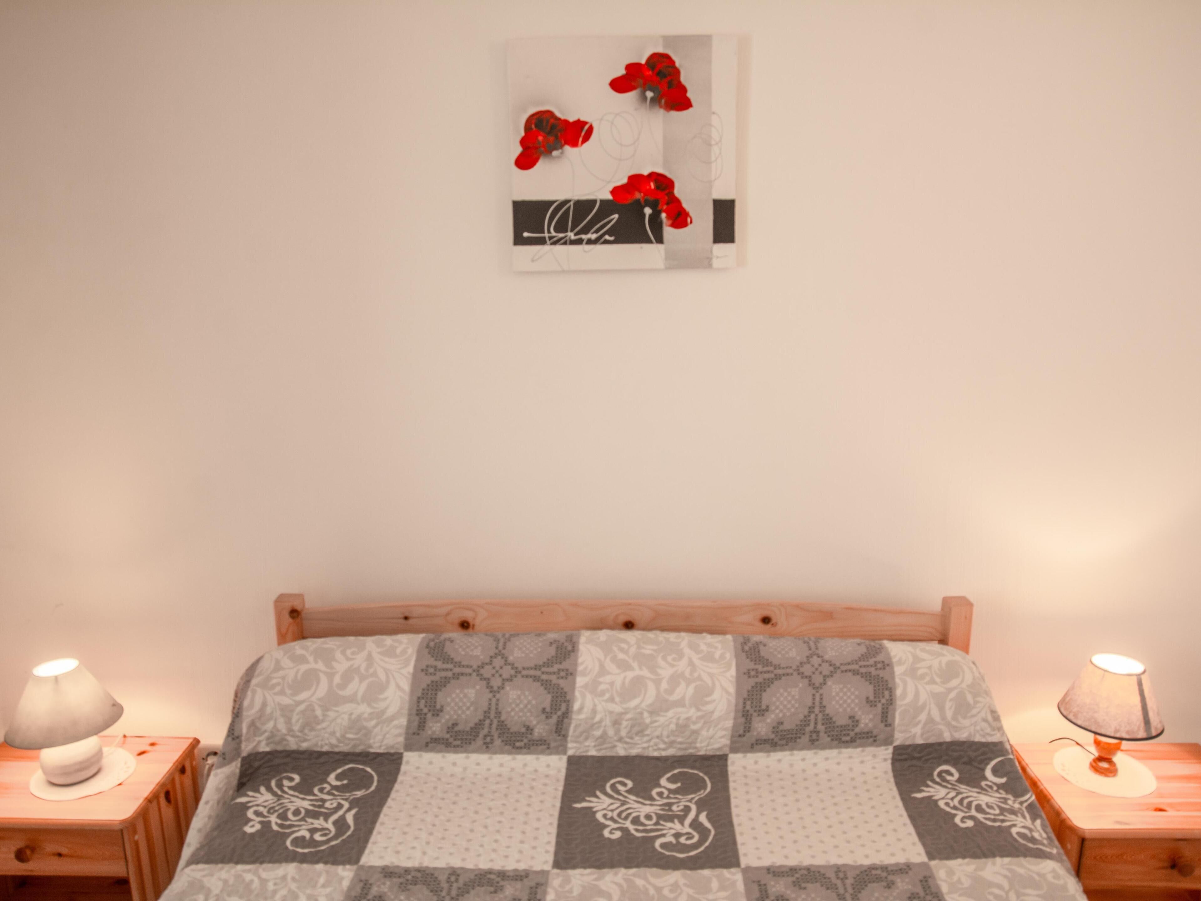 Ein Schlafzimmer mit einem hölzernen Bett, einer Bettdecke mit Karomuster, zwei Nachttischen mit Lampen und einem Wandbild über dem Bett.