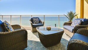 A balcony with wicker furniture, a glass coffee table, and a view of the ocean.