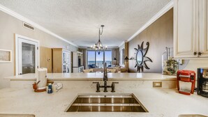 A kitchen with a stainless steel sink, a coffee maker, and a view to the living area.