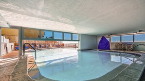 An indoor swimming pool with clear blue water, a tiled deck, and a view of the outside.
