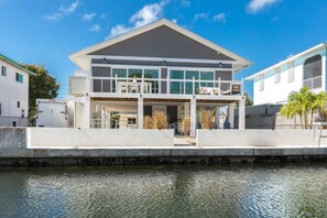 A modern two-story house with a balcony, a pool, and a view of the water.