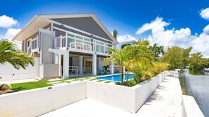A modern two-story house with a swimming pool, white exterior, and a view of a body of water. - The Salty Sailfish: Live the Keys Life, Stunning Canal Front Home, Pool, Dock & Dog-Friendly Bliss! (Summerland Key)