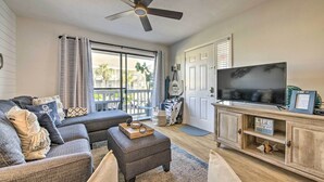 A living room with a grey sofa, ottoman, and a wooden entertainment unit with a TV. - PCB Condo Rental w/ Pool Access, Steps to Beach! (Panama City Beach)