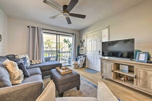 A living room with a grey sofa, ottoman, and a wooden entertainment unit with a TV.