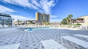 A pool area with hexagonal tiles, white lounge chairs, and a tall building in the background. - PCB Condo Rental w/ Pool Access, Steps to Beach! (Panama City Beach)