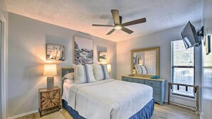 A bedroom with a bed, bedside tables, a ceiling fan, artwork on the walls, and a window with blinds. - PCB Condo Rental w/ Pool Access, Steps to Beach! (Panama City Beach)