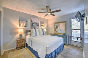 A bedroom with a bed, bedside tables, a ceiling fan, artwork on the walls, and a window with blinds.
