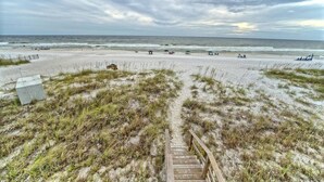 A beach with a wooden staircase leading down to the sand, grassy dunes, and the ocean in the background.