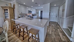 A modern kitchen with white cabinetry, a large island with stools, and a wooden floor.