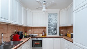 A kitchen with white cabinets, a built-in oven, a coffee maker, and a painting on the wall. - Apartment 'Bella Vista Marinella 1' with sea view, terrace, air conditioning and Wi-Fi (Olbia)