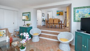 A living room with wicker chairs, a glass coffee table, a TV, and a dining area with a table and chairs. - Apartment 'Bella Vista Marinella 1' with sea view, terrace, air conditioning and Wi-Fi (Olbia)