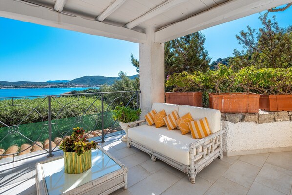 A balcony with a white sofa, potted plants, and a view of the sea.