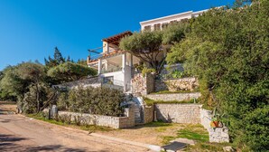 Una villa en la ladera con fachada de piedra, un balcón y abundante vegetación.