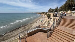 A beach with a staircase leading down to the shore, palm trees, and a clear sky.