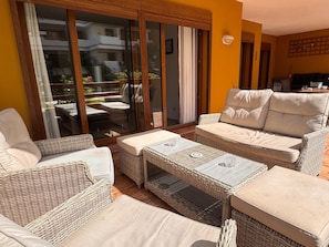 Un espace extérieur lumineux, aménagé pour être utilisé comme coin salon, avec des meubles en osier et une porte vitrée donnant sur un balcon.