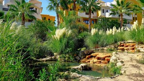 A coastal resort with palm trees, a rocky stream, and Mediterranean-style buildings.