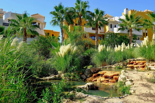 Un resort costero con palmeras, un arroyo rocoso y edificios de estilo mediterráneo.