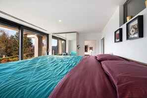 Une chambre avec un grand lit, une vue par une porte coulissante et un tableau encadré au mur.
