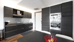 Une cuisine moderne avec des meubles en bois foncé, des appareils électroménagers en acier inoxydable et un coin repas comprenant une table noire et une chaise rouge.