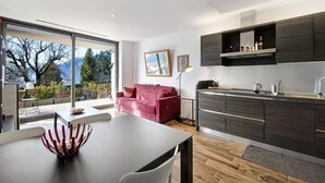 Une cuisine moderne avec des meubles en bois foncé, un coin repas agrémenté d’un canapé rouge et une grande fenêtre offrant une vue sur les arbres et les montagnes.