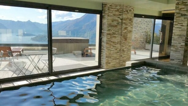 Un espace spa avec une piscine, un coin salon avec des fauteuils et une vue sur les montagnes et un lac.