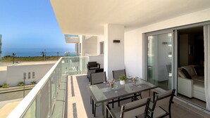 A balcony with a glass table, chairs, and a view of the ocean.