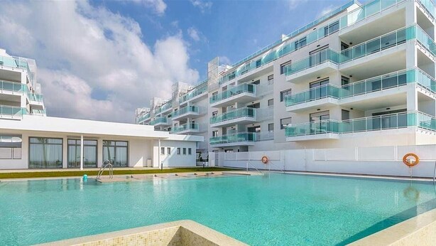 A modern hotel with a swimming pool, multiple balconies, and a clear sky.