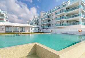 Un hotel moderno con piscina, varios balcones y cielo despejado.