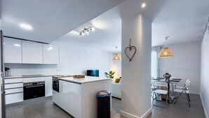 A modern kitchen with white cabinetry, a central island, and a dining area with a table and chairs.