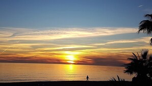 En solnedgång över ett stilla hav, med en silhuett av en person som promenerar längs stranden.