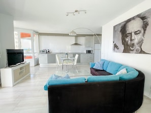 A modern living room with a black sofa, a glass coffee table, and a TV on a white cabinet.