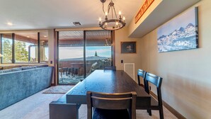 Un espace repas avec une grande table en bois, des chaises et un lustre. De grandes fenêtres offrent une vue sur une montagne enneigée.