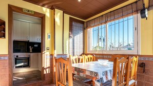 A dining area with a table and chairs, a kitchen with appliances, and a window with blinds. - Chalet 'Casa Thaiker' with Mountain Views, Garden, BBQ & A/C (Miami playa.  Tarragona)
