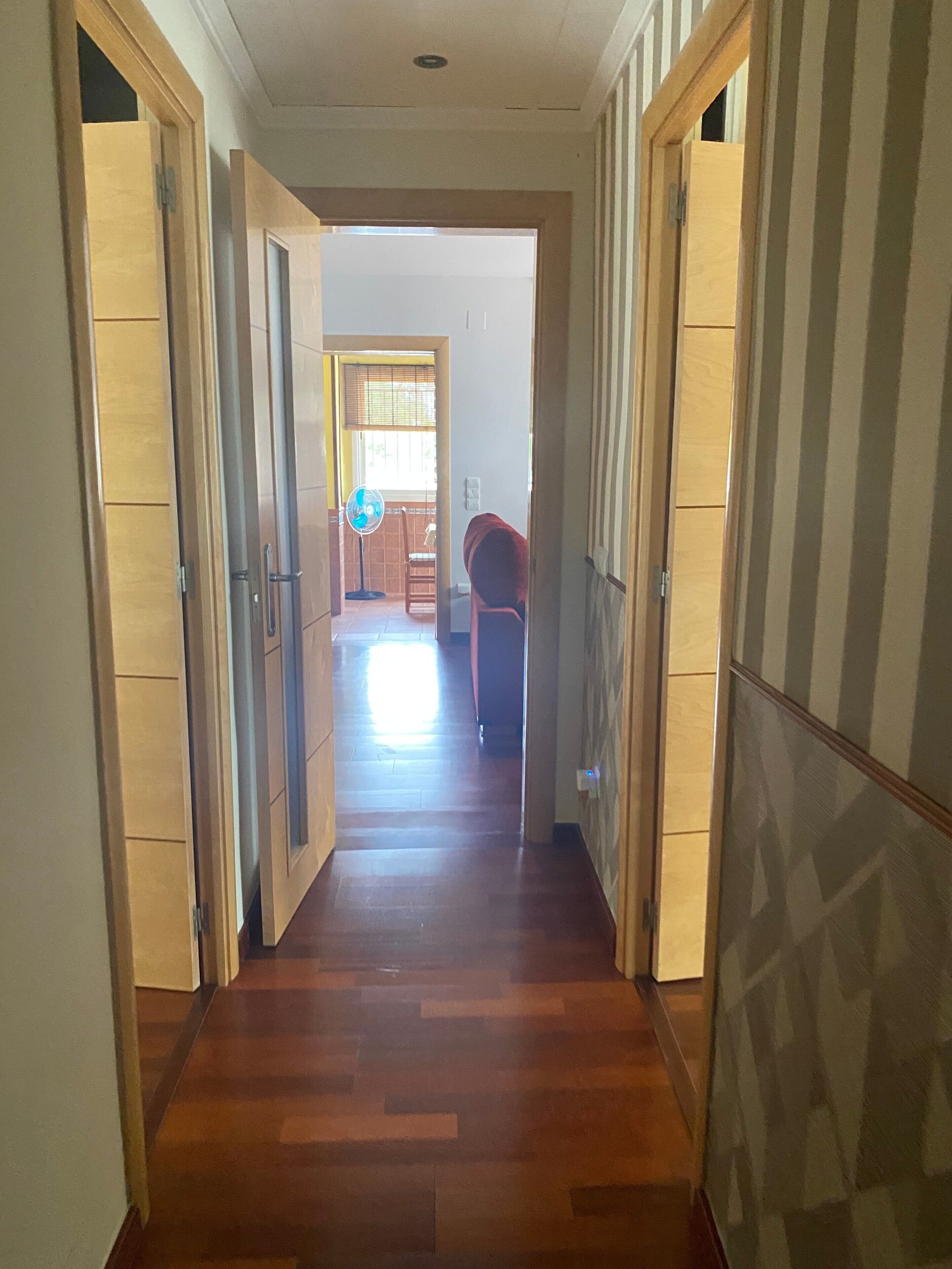 A hallway with wooden flooring, a fan, and a chair.