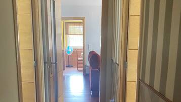 A hallway with wooden flooring, a fan, and a chair.