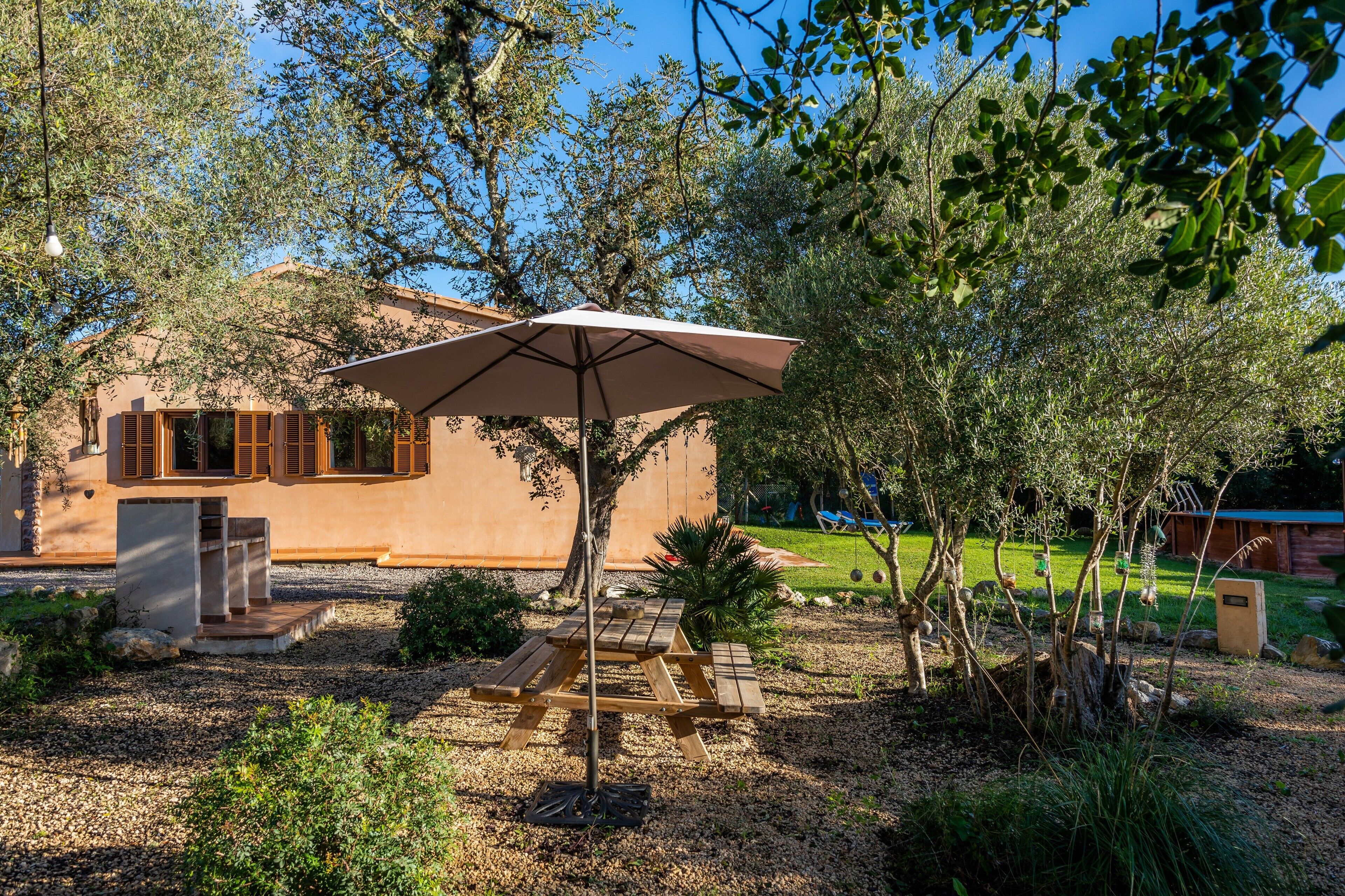 Un patio con mesa y sombrilla, rodeado de árboles y un edificio.