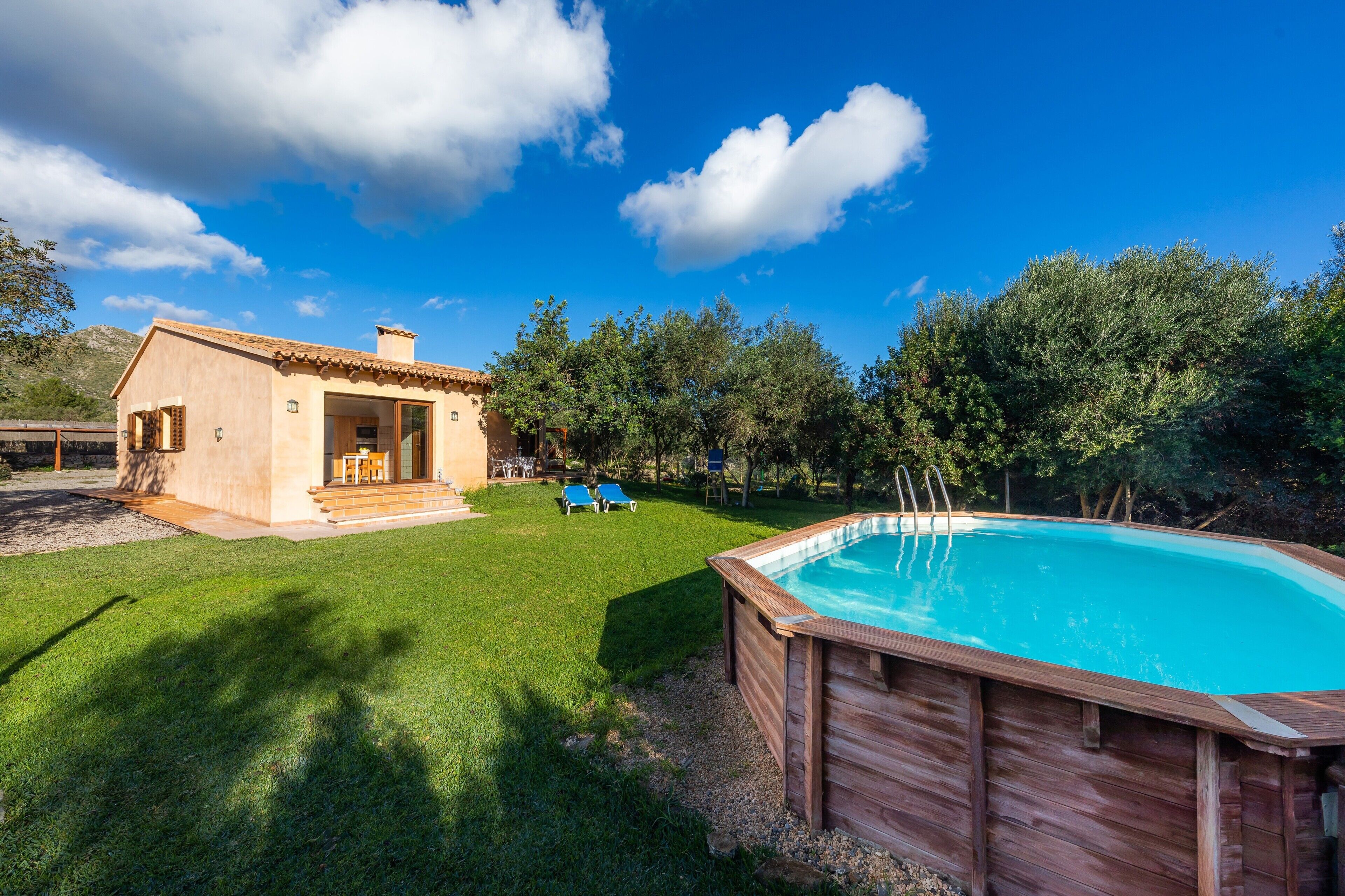 Una casa con piscina, un patio con dos sillas y vista a árboles.